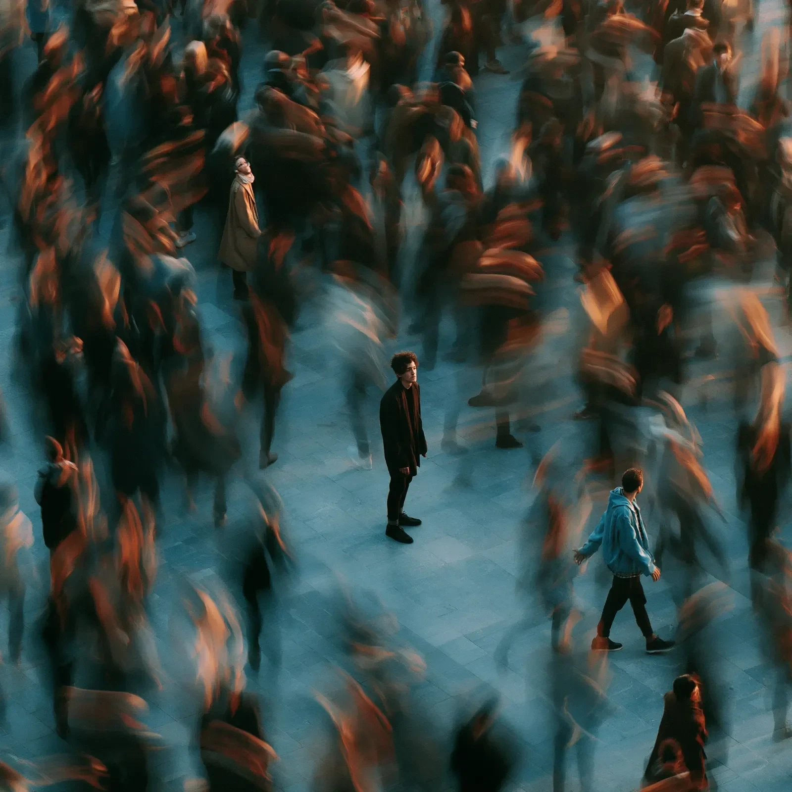 A lone figure stands still as a crowd hurries past